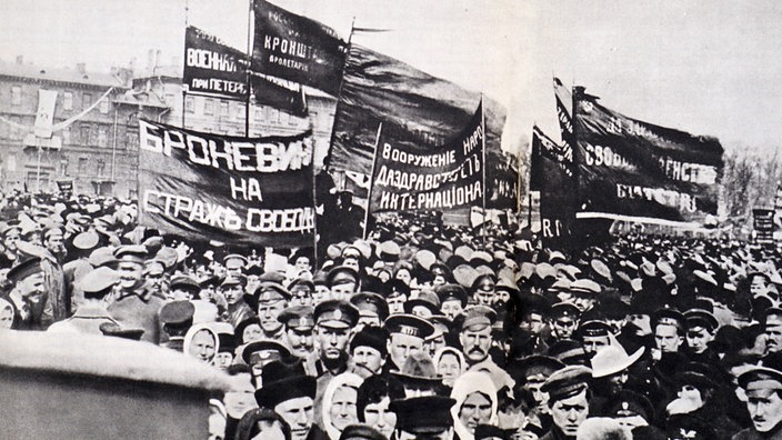 Schwarzweißaufnahme: Eine demonstrierende Menschenmenge mit Plakaten in russischer Schrift.