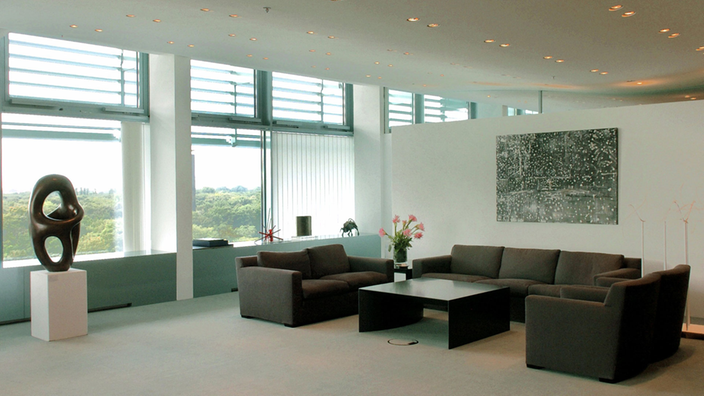 Großes Zimmer mit Blick auf den Reichstag, links ein schwarzer Schreibtisch, rechts ein Tisch mit mehreren Stühlen.