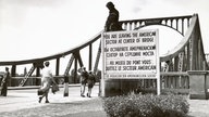 Das Schwarzweißbild zeigt eine Brücke, über die Fußgänger gehen.