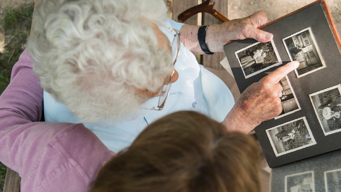 Alte und junge Frau sitzen auf einer Bank und schauen ein Fotoalbum an 	