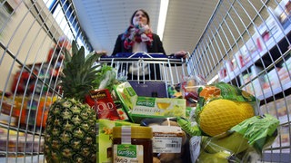 Eine Frau schiebt ihren gefüllten Einkaufswagen durch einen Supermarkt.