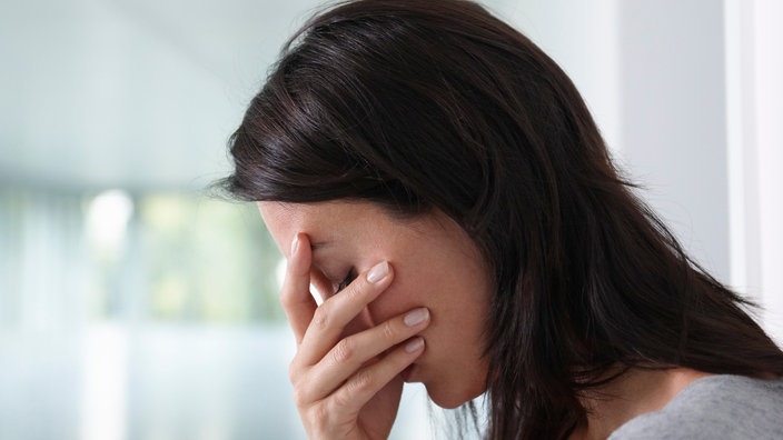 Eine dunkelhaarige Frau hat ihre Hand vor das Gesicht gelegt, sie wirkt erschöpft und enttäuscht