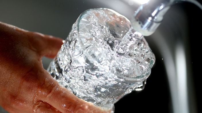 Jemand füllt Wasser in ein Glas, das überläuft.