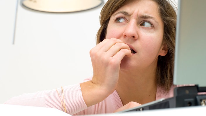 Eine Frau sitzt am Laptop und kaut an den Fingernägeln.