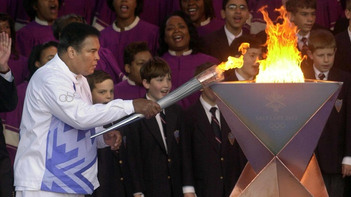 Muhammad Ali im Trainingsanzug entzündet mit einer Fackel eine Flamme.