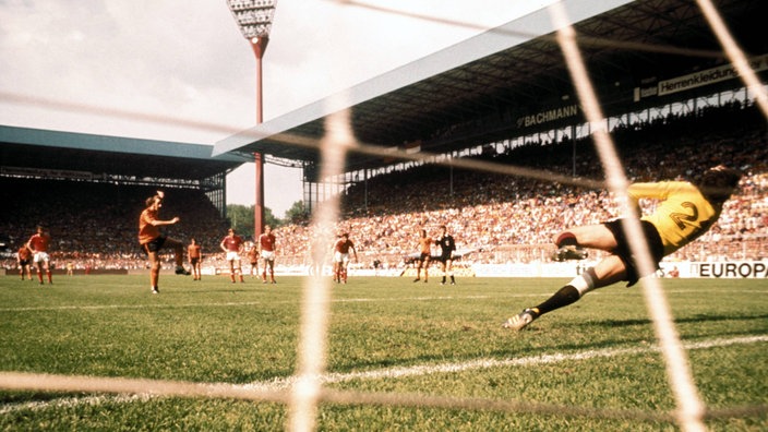 Spielsituation von hinten: Ein holländischer Spieler schießt gerade einen Elfmeter in die linke Ecke des Tores.