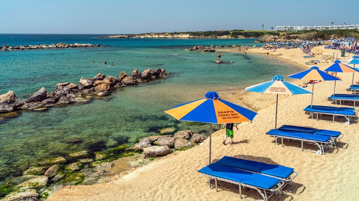 Ein Strand mit Sonnenschirmen und Liegen, im Hintergrund das Meer