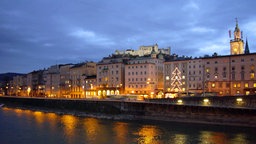 Salzburger Altstadt mit herausragenden Kirchentürmen in der Abenddämmerung. Auf einer Anhöhe die große Burganlage.