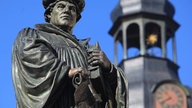 Denkmal des Reformators Martin Luther auf dem Marktplatz mit dem Turm der St. Andreaskirche im Hintergrund