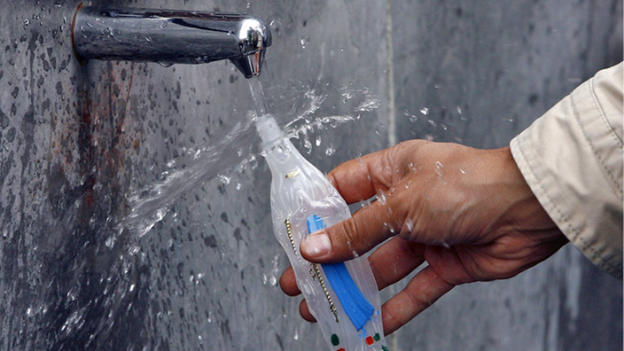 Hand füllt Wasser in Flasche ab.