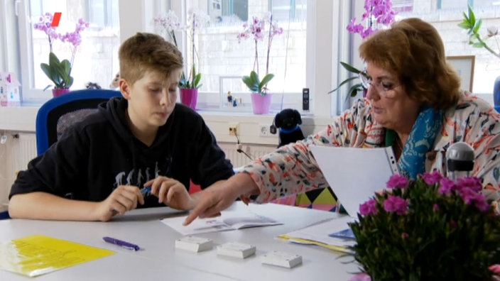 Ein Junge und eine Frau sitzen an einem Tisch und bearbeiten Schulaufgaben