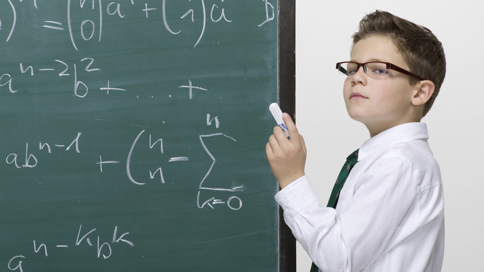 Ein Junge mit Schlips steht neben einer Tafel mit Matheformeln 