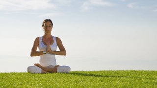 Eine Frau macht auf einer Wiese Yogaübungen