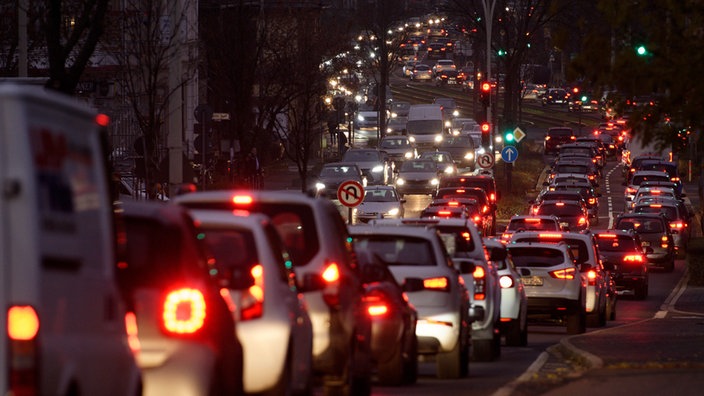 Sehr dichter Abendverkehr in beide Richtungen auf einer großen innerstädtischen Straße. Alle Autos haben das Licht an