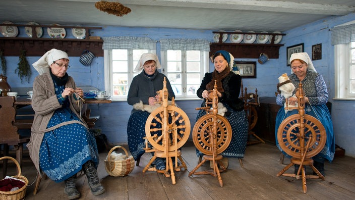 Frauen in Spreewälder Arbeitstracht sitzen an Spinnrädern und verarbeiten Schafwolle.